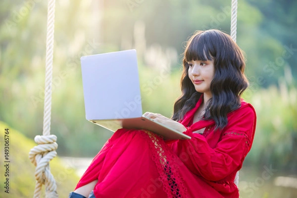 Obraz Beautiful confident asian businesswoman working with laptop, Hands typing keyboard. Online chat. Spend free time on the swing. Sunrise beam in the beautiful park.