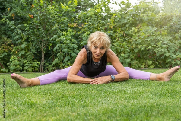Obraz Flexible smiling mature woman  doing a leg split outside. Horizontally. 