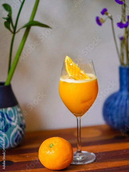Fototapeta Orange juice. A glass of fresh orange juice mocktail with ice on wooden table. Refreshment for summer.