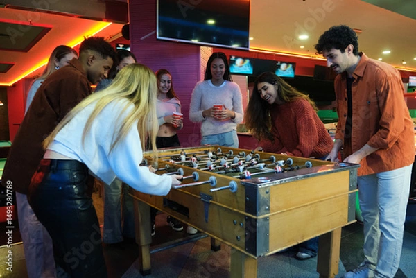 Obraz Group of young adults enjoying a foosball game in a lively arcade setting