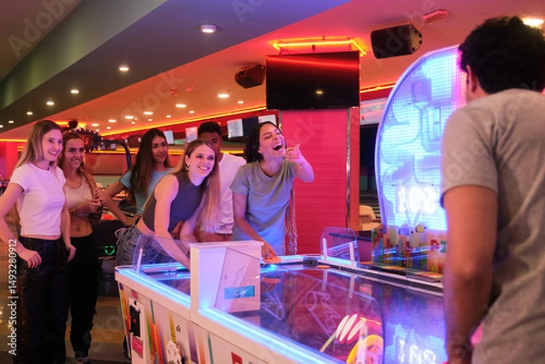 Obraz Group of young people playing air hockey, laughing and enjoying their time together in a colorful arcade