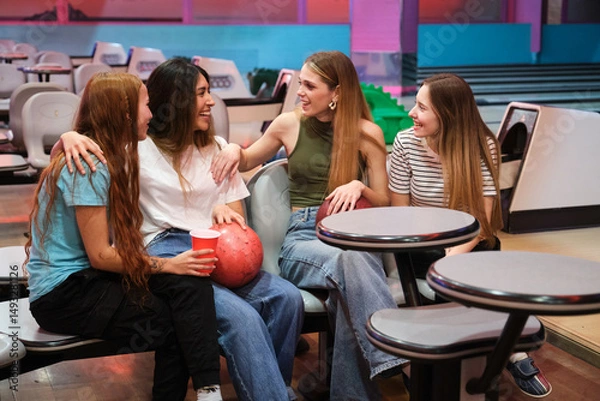 Obraz Four friends enjoying time together at bowling alley, chatting and having drinks