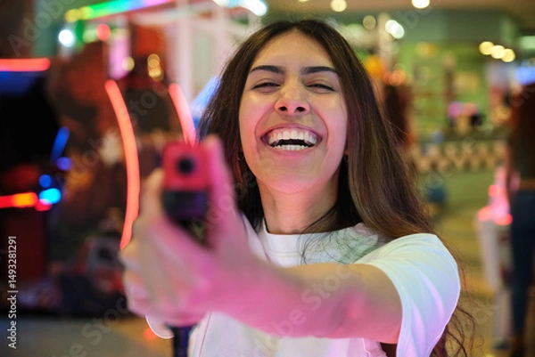 Obraz Young woman playing and laughing with toy gun in amusement arcade