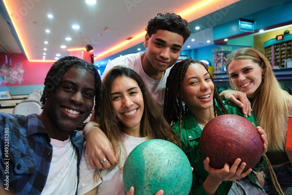 Obraz Five young multi ethnic friends are taking a selfie while holding bowling balls and smiling at the bowling alley