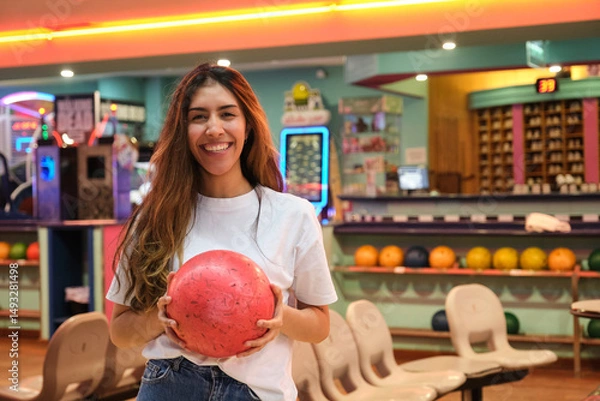 Obraz Happy woman holding a red bowling ball, smiling in a bowling alley