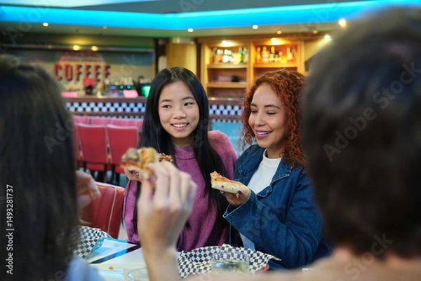 Obraz Group of friends sharing slices of pizza, laughing and having fun during a meal at a restaurant