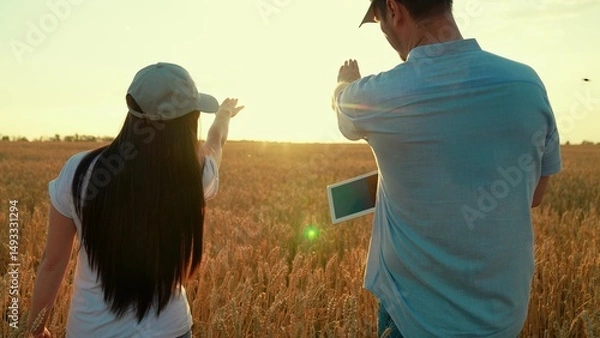 Obraz Two farmers shake hands with computer tablet, conclude contract in wheat field, sun. Work in team of business partners. Handshake of man of woman on field. Harvest, sale of grain Agricultural industry