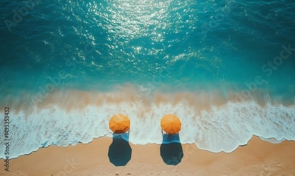 Fototapeta Aerial view of two orange umbrellas on a sandy beach with turquoise waves gently lapping the shore, creating a tranquil and inviting atmosphere