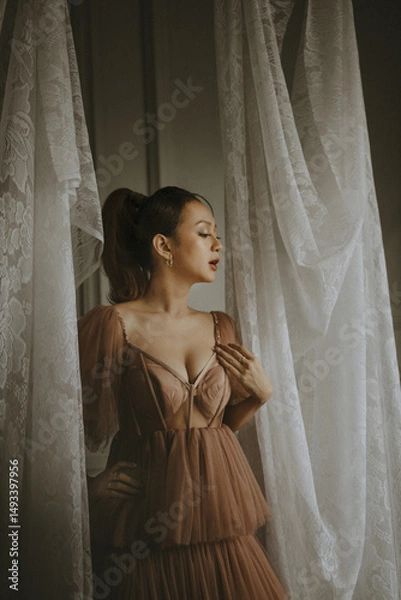 Obraz Elegant woman in a brown dress posing near white curtains in a graceful studio setting