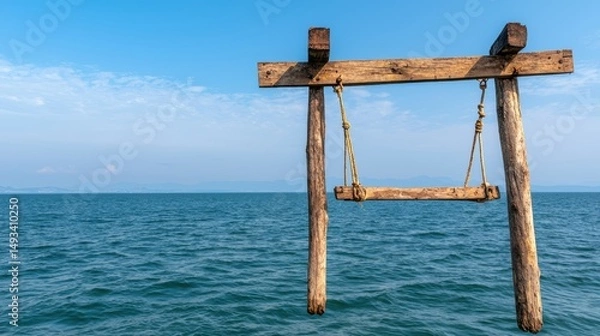 Fototapeta Wooden swing hanging from a rustic frame over calm blue ocean waters under a clear sky