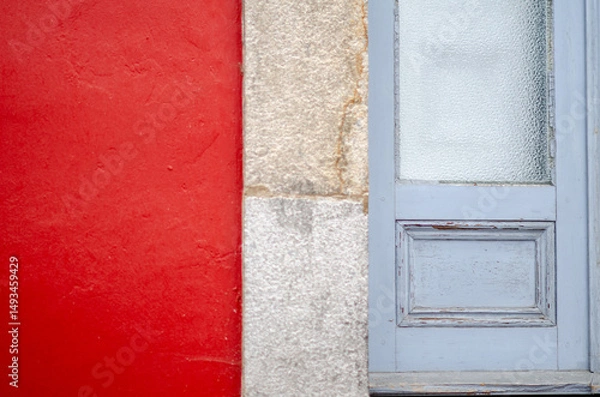 Fototapeta Close-up of a vibrant red wall next to an old blue wooden door with frosted glass, showcasing modern city minimalism and architectural details.