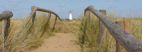 Fototapeta A wooden fence and board walk with a lighthouse in the background
