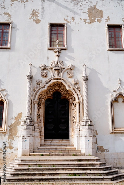Fototapeta A historic building with a grand entrance featuring ornate architectural details. The facade shows signs of wear with peeling paint, and the entrance is flanked by decorative columns and windows.