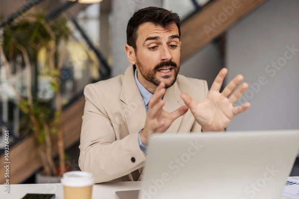 Fototapeta Portrait of corporate worker sitting at office and having conference call with associates on laptop.