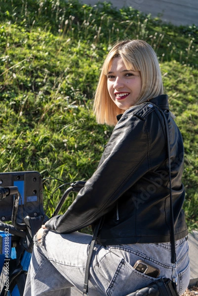 Fototapeta Young woman sitting on bike smiling at viewer in urban park