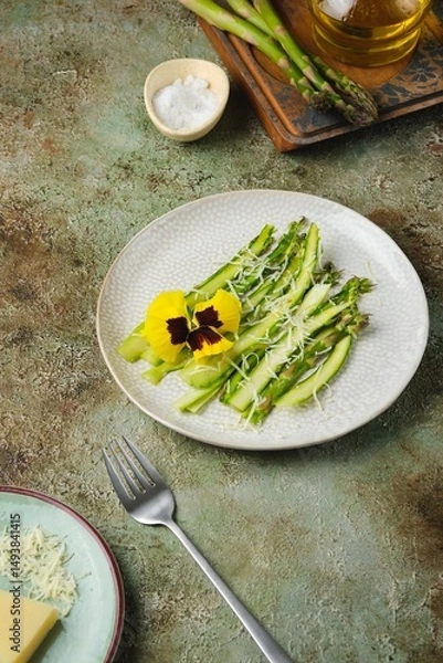 Fototapeta Appetizer, fresh asparagus carpaccio with parmesan cheese on a light plate on a green concrete background. Recipes asparagus.