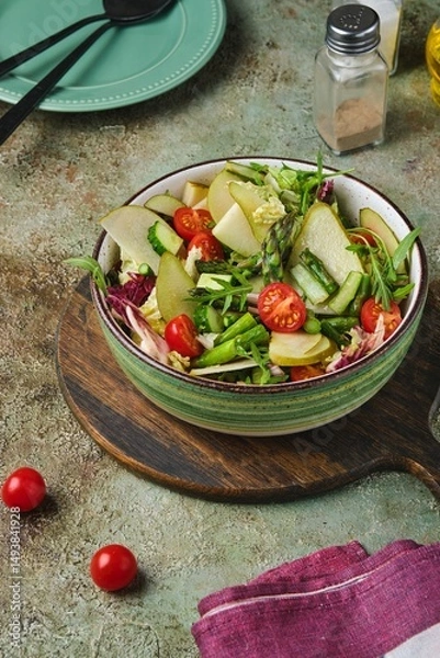 Fototapeta Fresh vegetable salad with fried asparagus, arugula, cucumber and cherry tomatoes in a green salad bowl on a green concrete background. Vegetable salads.