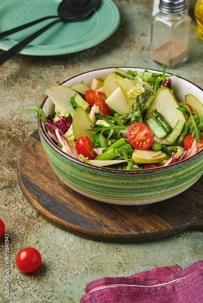 Fototapeta Fresh vegetable salad with fried asparagus, arugula, cucumber and cherry tomatoes in a green salad bowl on a green concrete background. Vegetable salads.