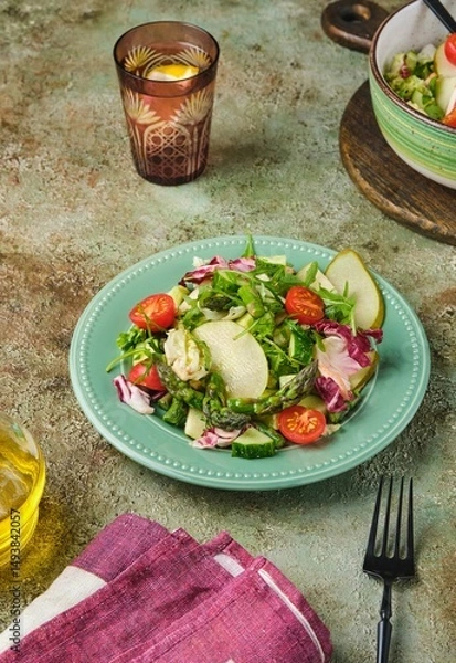 Fototapeta Fresh vegetable salad with fried asparagus, arugula, cucumber and cherry tomatoes on a green plate on a green concrete background. Vegetable salads, vegan recipes. Seasonal vegetables.