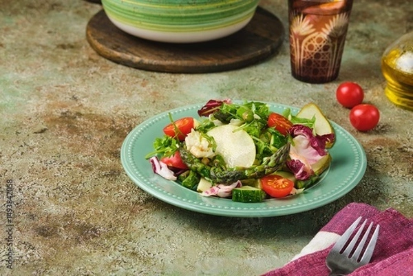 Fototapeta Fresh vegetable salad with fried asparagus, arugula, cucumber and cherry tomatoes on a green plate on a green concrete background. Vegetable salads, vegan recipes. Seasonal vegetables.