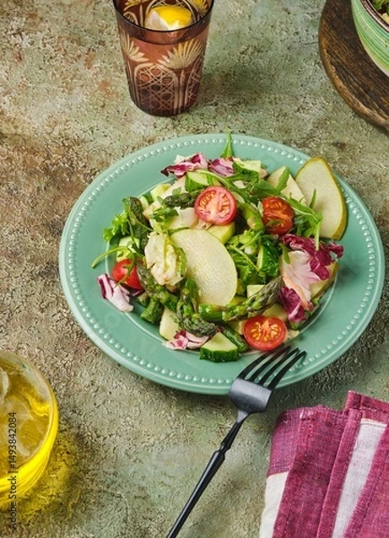Fototapeta Fresh vegetable salad with fried asparagus, arugula, cucumber and cherry tomatoes on a green plate on a green concrete background. Vegetable salads, vegan recipes. Seasonal vegetables.