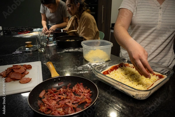 Obraz Three unrecognizable women collaborate in a kitchen, making pizza, food using dough and molds