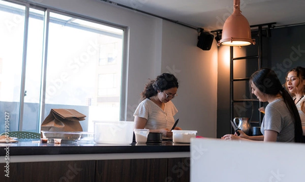 Obraz Three friends collaborate in a modern kitchen, engaging in cooking and enjoying lively conversation with copy space