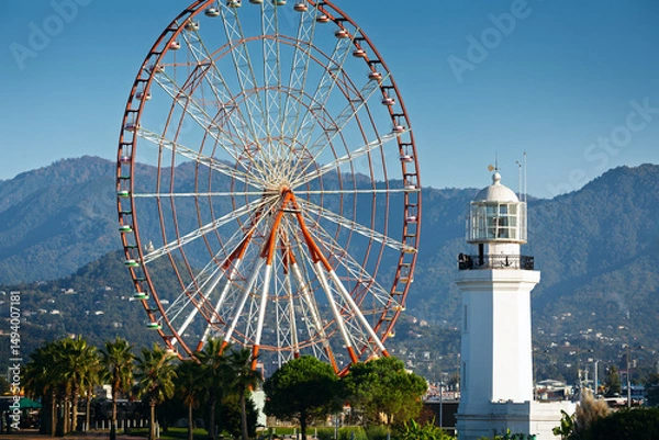 Fototapeta View of the observation wheel and lighthouse against a mountain backdrop in Batumi, Georgia