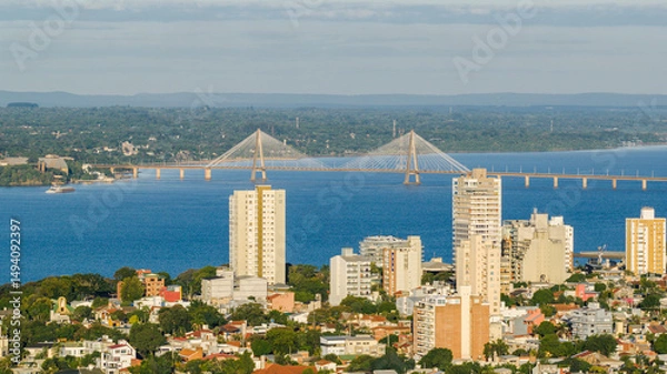 Obraz Daytime view of downtown Posadas, Argentina, with the San Roque González de Santa Cruz Bridge over the Paraná River in the background.