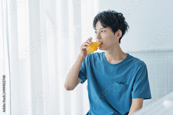 Fototapeta 朝にオレンジジュースを飲む若い男性