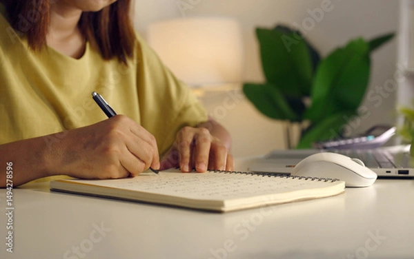 Fototapeta Asian woman works from home, surrounded by notes, a laptop, and messages. She browses the internet, writes ideas, and researches for her startup, utilizing wireless technology.