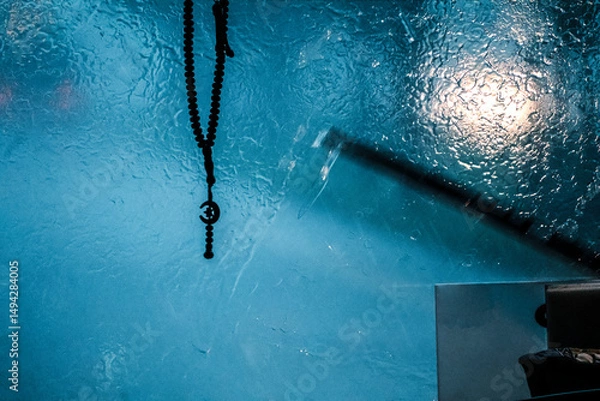 Obraz View from the windshield of a car during the rain. A Muslim rosary with a crescent moon hangs in front of the glass. Poor visibility while driving on the road. Tropical downpour, raindrops on glass