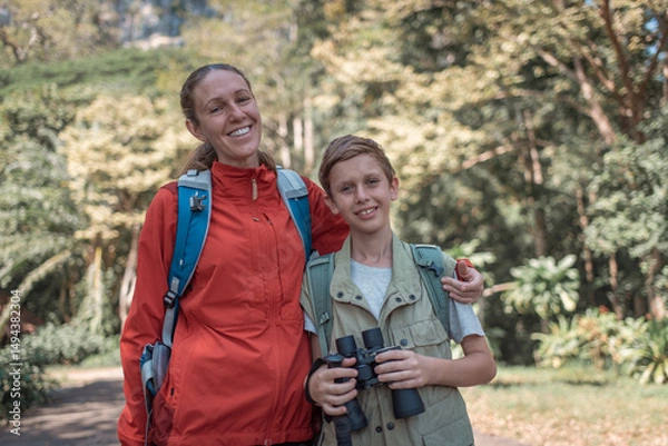Fototapeta Hikers or explorers family on journey carrying backpack, trekking poles and holding binoculars looks into the distance observing guide trekking and trail exploration holiday ecotourism concept