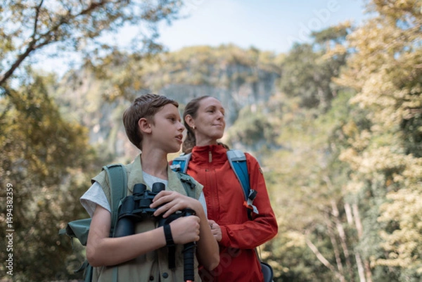 Fototapeta Hikers or explorers family on journey carrying backpack, trekking poles and holding binoculars looks into the distance observing guide trekking and trail exploration holiday ecotourism concept