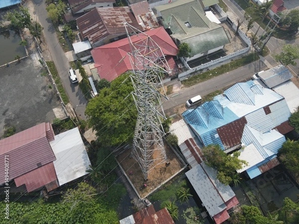 Obraz Electricity generated from generation is distributed through transmission towers before reaching consumers. Transmission towers pass on the roof of densely populated residential house in a city