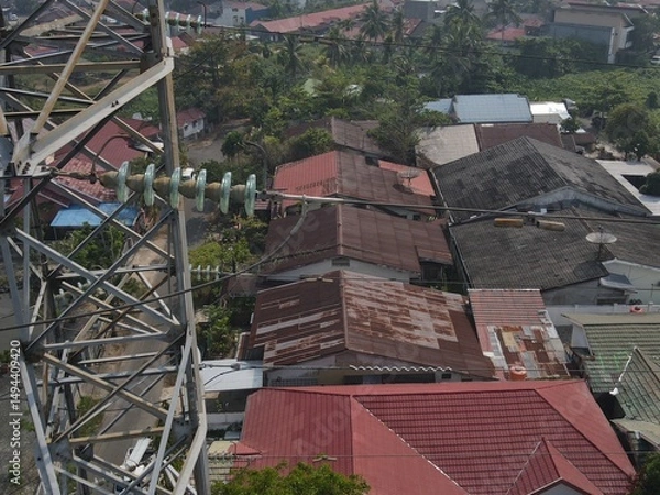 Obraz Electricity generated from generation is distributed through transmission towers before reaching consumers. Transmission towers pass on the roof of densely populated residential house in a city