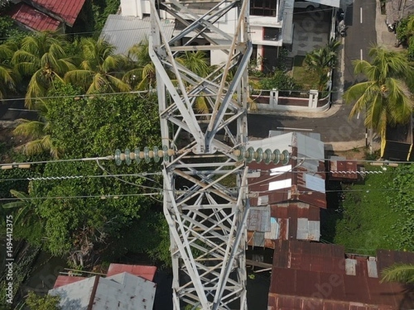 Obraz Electricity generated from generation is distributed through transmission towers before reaching consumers. Transmission towers pass on the roof of densely populated residential house in a city