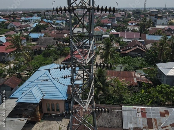 Obraz Electricity generated from generation is distributed through transmission towers before reaching consumers. Transmission towers pass on the roof of densely populated residential house in a city