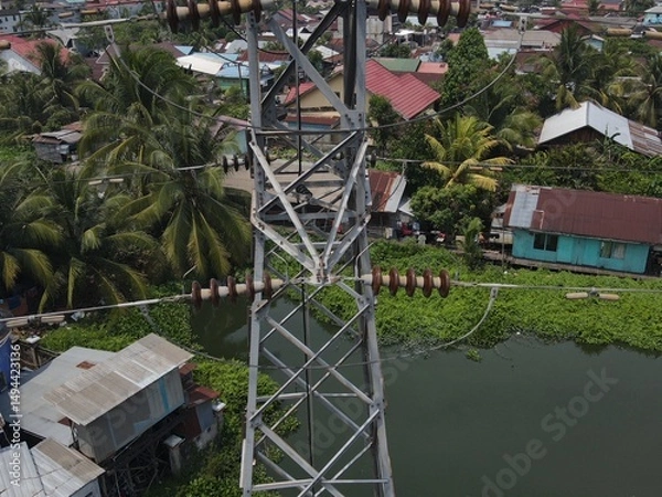 Obraz Electricity generated from generation is distributed through transmission towers before reaching consumers. Transmission towers pass on the roof of densely populated residential house in a city