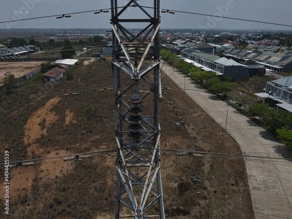 Obraz Electricity generated from generation is distributed through transmission towers before reaching consumers. Transmission towers pass on the roof of densely populated residential house in a city