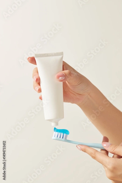Fototapeta Minimalist image showing hands applying toothpaste onto a blue toothbrush. Ideal for dental ads, morning routine concepts, or healthcare visuals.