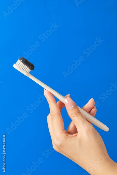 Fototapeta A hand is holding a toothbrush with black bristles. The background is bright blue. The toothbrush looks modern and simple. This image is great for oral care ads or minimalist product photos.