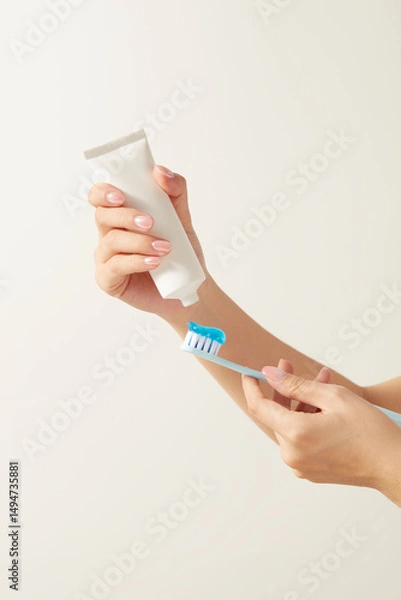 Fototapeta Close-up shot of two hands holding a toothbrush and squeezing white toothpaste from a simple white tube.  Perfect for promoting toothpaste, dental products, or healthy lifestyle content.