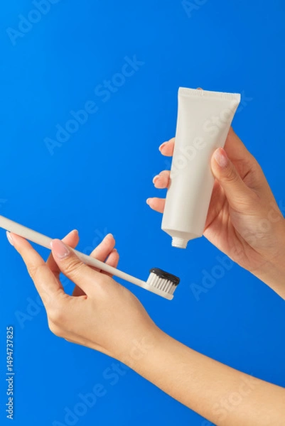 Fototapeta One hand is holding a toothpaste tube, and the other hand is holding a toothbrush. The image is taken with a blue background. It shows a daily brushing habit. 