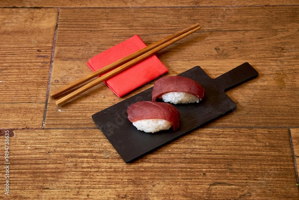 Obraz A plate of sushi with chopsticks and napkins on a wooden table. The sushi is cut into two pieces