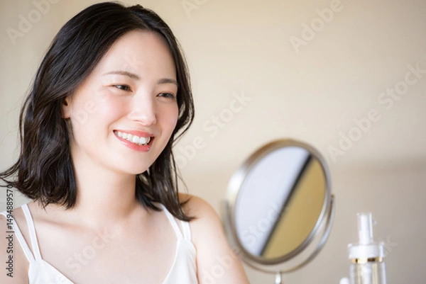 Fototapeta 鏡をみる素肌感が美しい若い女性の美容やビューティーイメージクローズアップ　ベージュや黄色背景	