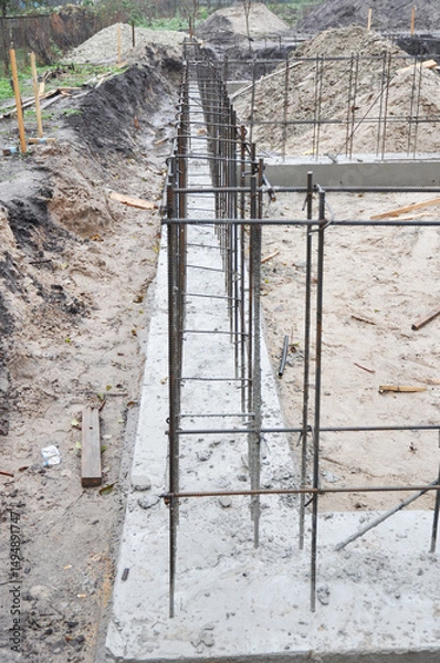 Fototapeta Strip foundation construction close up. House concrete foundation with reinforced footing trenches, rebars installed and concrete poured.