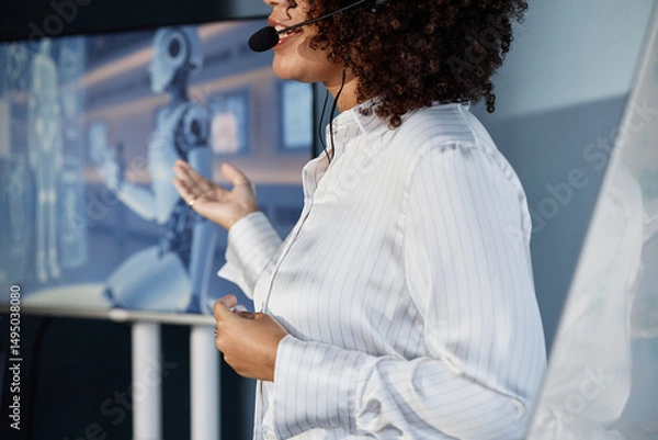 Fototapeta Cropped shot of female speaker wearing headset microphone leading talk on AI technology integration into modern business pointing at presentation on screen during professional conference
