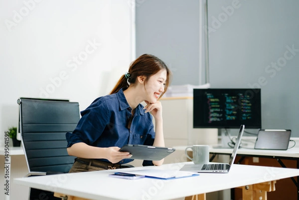 Obraz Young female programmer working with tablet and screen displaying code. Modern tech office setup, great for software, coding, IT