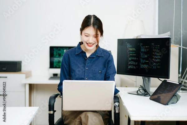 Fototapeta Young female programmer working with tablet and screen displaying code. Modern tech office setup, great for software, coding, IT